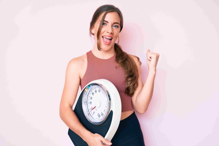 Woman holding weigh Machine and Smiling after Vaginal Rejuvenation | Santee, CA